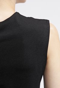 Czarny top bez rękawów wykonany z teksturowanej tkaniny, z konstrukcyjnym designem na ramionach i gładkimi pachami, prezentujący minimalistyczny styl.