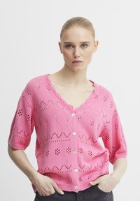 Ružový pletený sveter s krátkymi rukávmi, okrajom so zúbkami a dekoratívnymi vzormi. Obsahuje zapínanie na gombíky a textúrované detaily.