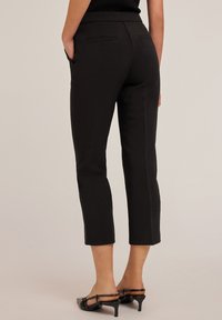 Zwarte cropped broeken met een gladde stofstructuur, een op maat gemaakte design en twee achterzakken. Afgewerkt met een subtiele plooival langs de voorkant van de benen.