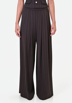 Pantalon large marron foncé à fines rayures verticales porté par une personne sur un fond clair uni.