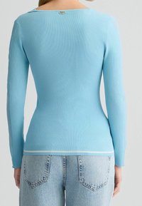 Haut à manches longues côtelé de couleur bleu clair avec un col arrondi. Il présente une discrète fermeture décorative à l'arrière et un accent blanc à l'ourlet.