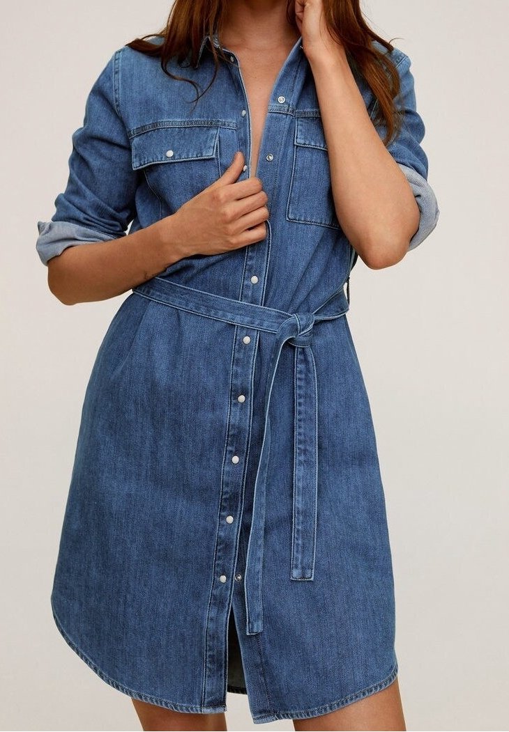 Robe chemise en denim bleu moyen avec un bouton devant, deux poches poitrine, manches retroussées et une ceinture assortie à la taille.