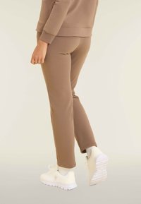 Pantaloni da jogging marroni, aderenti, realizzati in morbido tessuto, con un design tapered e cintura elastica. Abbinati a sneaker bianche e calzini alla caviglia.