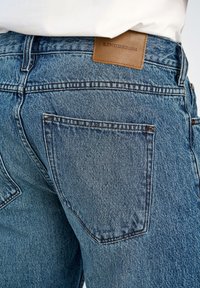 Jeans di denim blu a taglio dritto, con etichetta del marchio in pelle color cuoio e due tasche posteriori con cuciture rinforzate.