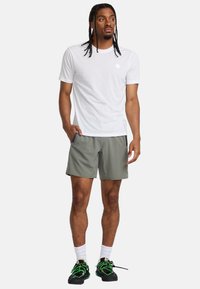 Vit kortärmad t-shirt med rund halsringning, kombinerad med olivgröna shorts och svarta sneakers med gröna snören. Enkelt design, utan mönster.