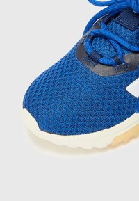 Scarpa da ginnastica blu con una tomaia in rete testurizzata, dettagli neri e una suola in gomma bianca. Presenta lacci prominenti e un design della punta arrotondato.