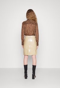 Majica s leopardjim vzorcem z dolgimi rokavi iz prosojnega materiala, v kombinaciji z sijočo bež usnjeno mini krilo in črnimi škornji do kolen s peto.