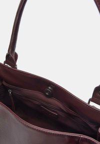 Bordowa skórzana torba typu tote o gładkiej fakturze, wyposażona w zapięcie na zatrzask oraz wewnętrzną kieszeń na zamek dla lepszej organizacji.