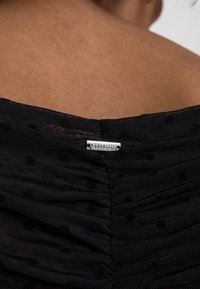 Tessuto nero a trama con pois in rilievo, con design arricciato e etichetta in metallo argentato sul retro del collo.