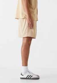 Chemise en mesh beige respirante assortie à un short, avec une coupe décontractée et une texture perforée subtile. Baskets blanches avec des accents noirs.