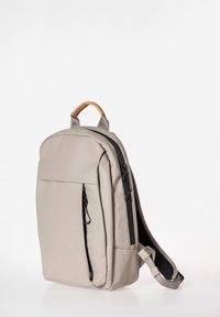 Beige rugzak met een gladde, matte afwerking en een contrasterende zwarte rits. Beschikt over een ergonomisch handvat en een verstelbare schouderriem.