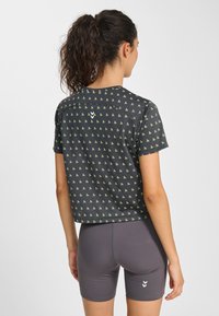 Svart skjorta med korta ärmar och små gröna mönster, tyget har en mjuk textur. Matchas med gråa sportshorts med vita detaljer.