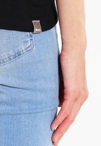 T-shirt en coton noir avec une étiquette Bench sur le côté, associée à un jean en denim bleu clair avec un design de poche arrière.