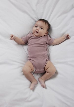 Beebi lamamas valgel voodil, seljas lilla lühikeste varrukatega bodi, vaadates tähelepanelikult, käed ja jalad kergelt kõverdatud ja laiali.