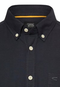 Navy button-up shirt with a collar, featuring cream buttons, yellow inner collar detail, and subtle stitching. Includes left chest logo.