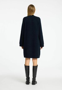 Jūras spēku zila trikotāža oversized kleita ar garām piedurknēm un apaļu kakla izgriezumu. Vilnai līdzīga tekstūra. Saskaņota ar melnām ādas zābakiem līdz ceļgaliem.