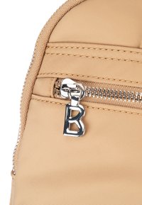 Bež tkaninska torba z teksturirano površino, opremljena s srebrnim zadrgo in obeskom zadrge v obliki črke "B".