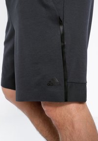 Pantalones cortos deportivos negros hechos de una tela suave con una franja de satén negra, que cuentan con un sutil logo de Adidas en el dobladillo y una textura perforada.
