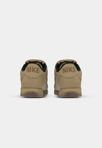 Adidași Nike bej cu accente negre, având un guler căptușit, talpă din cauciuc și logo debossat pe călcâi. Suport din piele texturată.