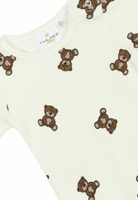 Hvid ribbet body med et all-over print af små brune bamser. Indeholder trykknapper ved skulderen for nem påklædning.