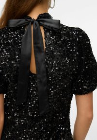 Melnas sekvīnām greznotas kleitas ar uzpūstām īsām piedurknēm, atvērtu muguru un melnu zīda lentu, kas sasieta ap kaklu, veidojot loku.