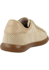 Sneaker in suede perforato beige con suola in gomma marrone e branding discreto sul tallone. Design con lacci e punta arrotondata.