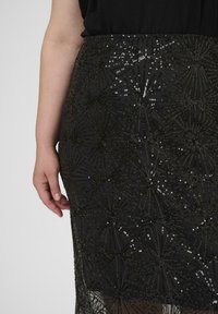 Jupe en sequins noirs avec une silhouette ajustée, présentant un motif géométrique de sequins scintillants et un tissu texturé. Design mi-long.