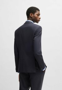 Giacca da abito blu navy con vestibilità su misura, dotata di due spacco posteriori, revers a occhiello e bottoni decorativi sulle maniche. Tessuto dalla superficie liscia.