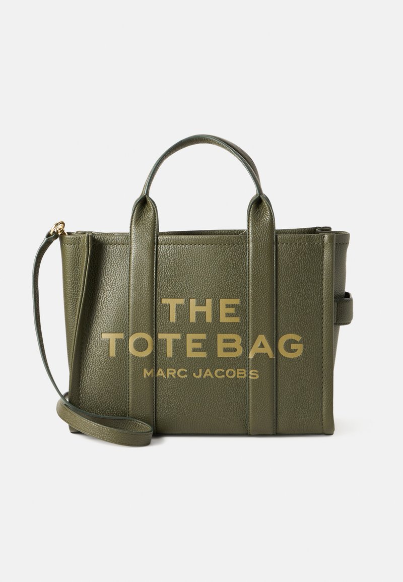 Alyvučių spalvos odinė rankinė su dviem viršutiniais rankenomis, nuimamu peties dirželiu ir auksinės spalvos užrašu "THE TOTE BAG MARC JACOBS."