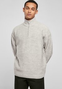 Lys grå pullover-sweater med høj krave og halv lynlås, med et struktureret strikkemønster samt ribbede manchetter og kant.
