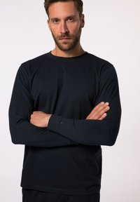Camicia a maniche lunghe di colore navy, realizzata in tessuto morbido, con scollatura rotonda e maniche aderenti, caratterizzata da dettagli di cuciture sottili ai polsini.