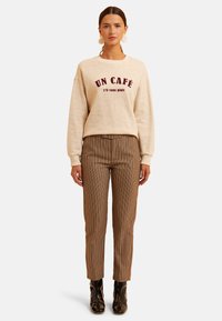 Sudadera beige con texto burdeos, combinada con pantalones de cuadros marrones. Tela de mezcla de poliéster, diseño ajustado y botas de tobillo negras brillantes.