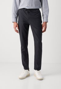 Dark navy, lightweight, stretch pants with an elastic waistband and drawstring. Paired with white sneakers and a striped shirt.