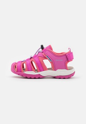 Sandalias rosas con un diseño de malla y goma, que cuentan con múltiples correas, una pestaña de tirón y una suela blanca con textura antideslizante.