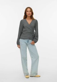 Svart och vit rutad wraptop med långa ärmar, V-ringning och detaljer med sidoknytning, kombinerad med ljusblå vida jeans och gula skor.
