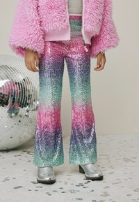 Shimmering pink, purple, and green sequin flared pants, paired with a fuzzy pink jacket and metallic silver boots. Mirror ball in background.