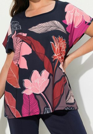 Femme portant un haut à manches courtes bleu marine avec de grands motifs floraux et de feuilles roses, rouges et violets.