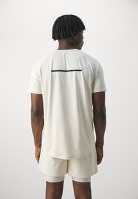 Camiseta deportiva color beige claro con raya horizontal negra en la parte posterior, hecha de un tejido transpirable, combinada con pantalones cortos a juego.