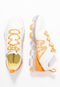 Vita sportskor i vitt med orange accenter, meshupplevation och transparent sula. Har elastiska snören, varumärke och texturerade överdrag.