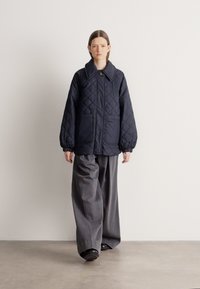 Κουκουλωμένο ναυτικό μπουφάν με μεγάλο γιακά, με δύο μπροστινές τσέπες και ελαστικά μανίκια, σε συνδυασμό με φαρδιά γκρι παντελόνια και μαύρα παπούτσια.