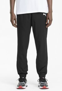 Sorte lette joggebukser med elastisk linning, tettsittende mansjetter og en liten hvit logo på venstre lår. Brukt med svart- og hvitfargede joggesko.