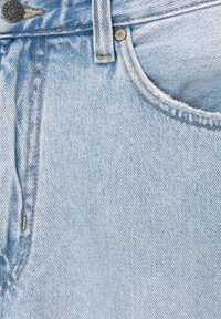 Tissu en denim bleu clair présentant un gros plan d'une taille, d'un bouton en métal et d'une poche, avec des coutures visibles et un bord légèrement effiloché.