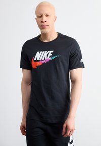 Črna bombažna majica s kratkimi rokavi, ki na sprednji strani nosi velik, barvit Nike logotip v gradientnem oblikovanju. Ima okroglo ovratnik.