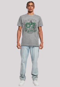 Grijze katoenen t-shirt met een groene grafische print met "MALFOY" en "07" boven een decoratief ontwerp. Gecombineerd met lichte denim jeans en witte sneakers.