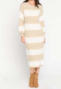 Stickad långärmad klänning med horisontella beige och vita ränder. Mjuk känsla, lös passform och rak silhuett, avslutad ovanför vaden.