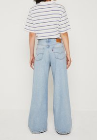 Svetle modré džíny s širokými nohavicemi vyrobené z denimu, s vysokým pasem, zadními kapsami a hnědou koženou značkovou nášivkou na pase.