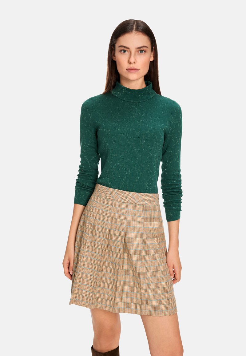 Grüner Rollkragenpullover aus strukturiertem Strick, kombiniert mit einem karierter A-Linien-Rock in Beige-, Orange- und Blautönen. Braune kniehohe Stiefel.