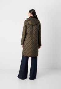 Olijfgroene gevoerde lange jas met capuchon, met een trekkoord in de taille en een diagonaal ruitpatroon, gecombineerd met wijde donkere denim broeken.