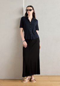 Navy short-sleeve button-up shirt paired with a black maxi skirt, textured sandals, and black sunglasses; minimalist and cohesive design.