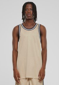 Beige netting tank topp med svart og hvit kant, med løs passform og uten ermer. Merkbar tekstur og pustende materiale.